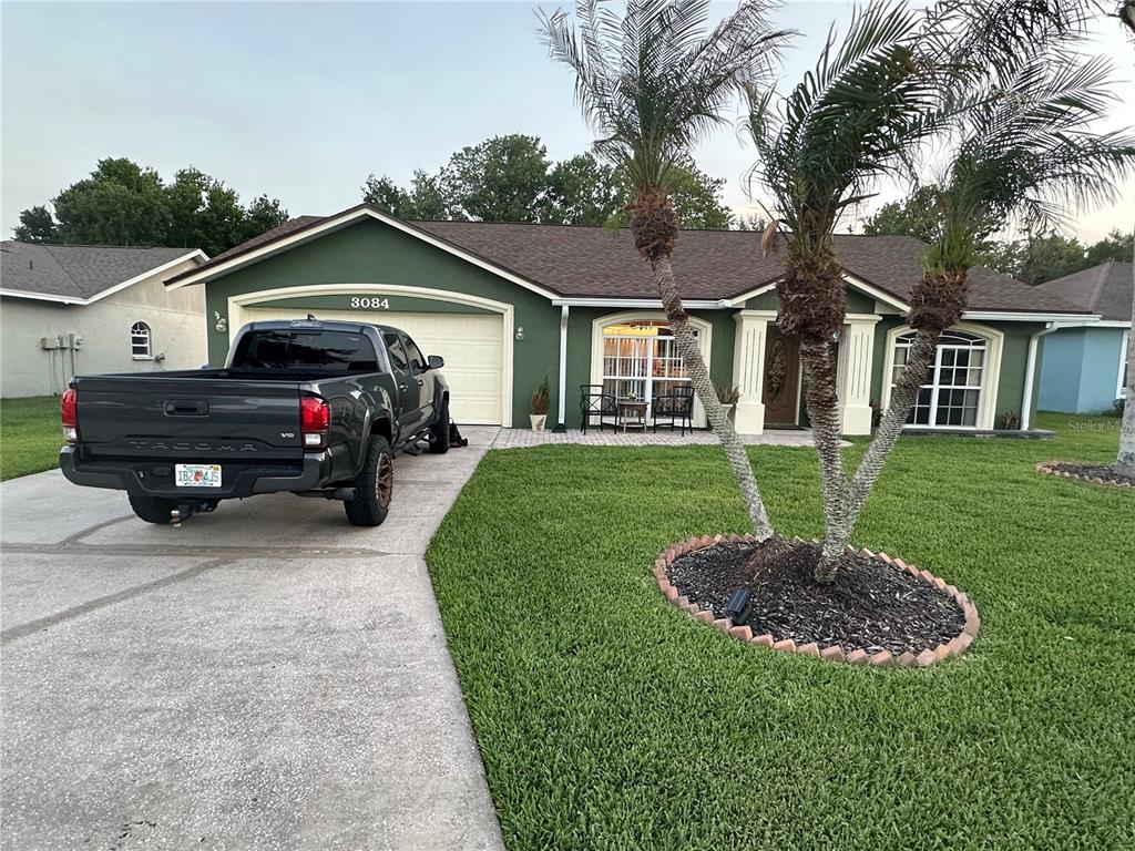 A single-story green house with a dark gray pickup truck parked in the concrete driveway — 3084 THOROUGHBRED LOOP W, LAKELAND, FL