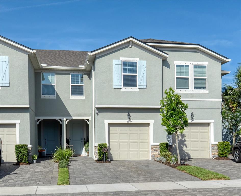 A two-story townhouse exterior features light gray stucco, tan garage doors, and blue shutters — 2507 ARBOR WIND DRIVE, LUTZ, FL