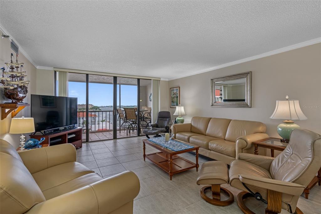 A living room with beige leather furniture, tile flooring, and a balcony overlooking the water — 19111 VISTA BAY DRIVE UNIT 612, INDIAN SHORES, FL