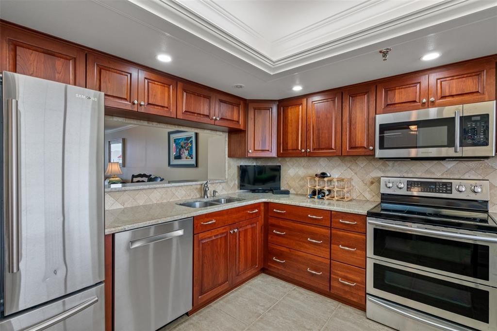 A kitchen with wood cabinets, stainless steel appliances, granite countertops, and a tile backsplash — 19111 VISTA BAY DRIVE UNIT 612, INDIAN SHORES, FL