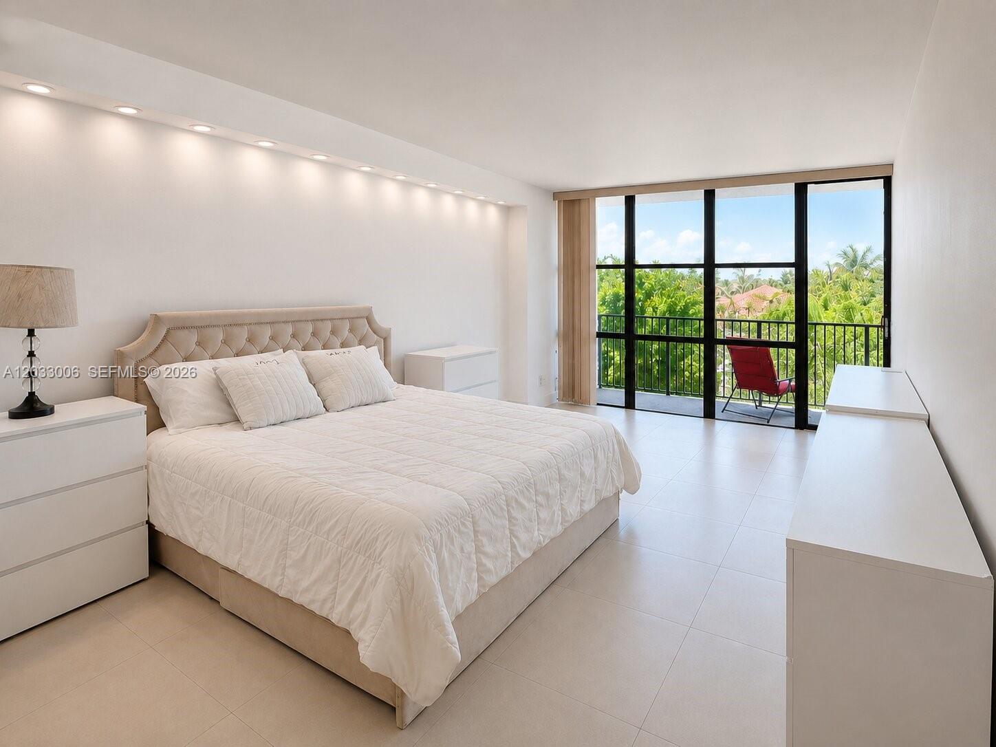 A bedroom features a tufted headboard, white furniture, recessed lighting, and a balcony with greenery — 1000 Parkview Dr # 415, Hallandale Beach FL 33009, HALLANDALE BEACH, FL