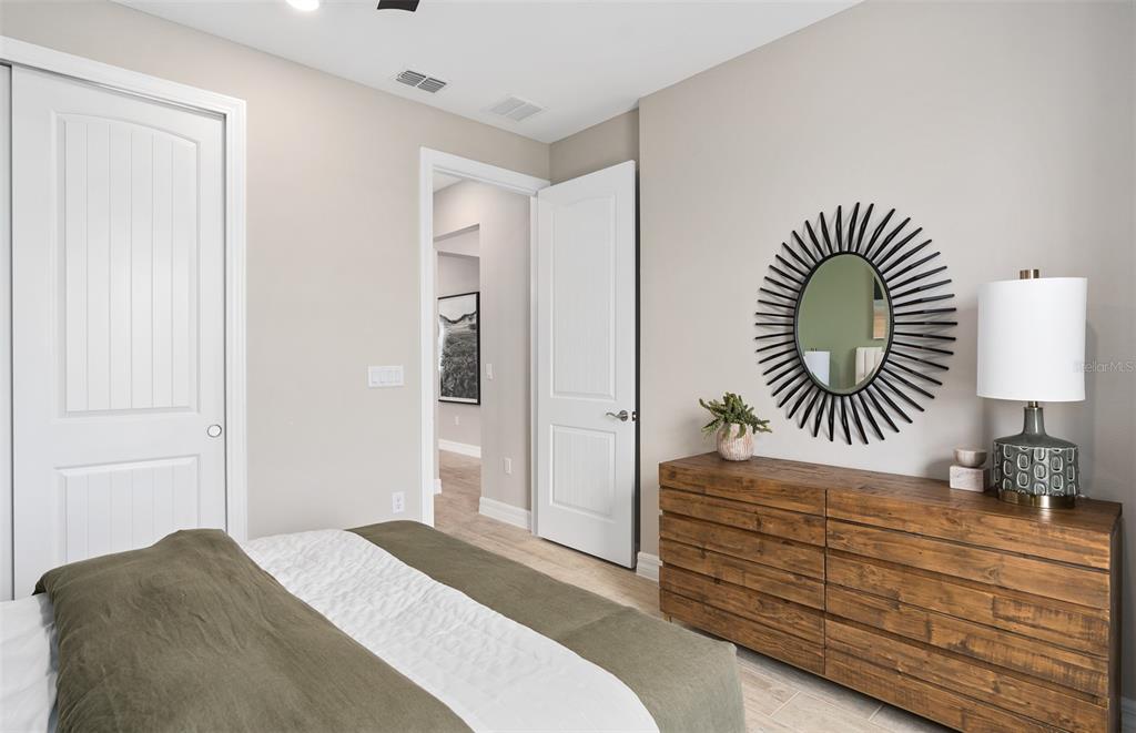 A bedroom features a wooden dresser, a sunburst mirror, and a doorway leading to a hallway — 6812 WILLOW BANK DRIVE, CLERMONT, FL