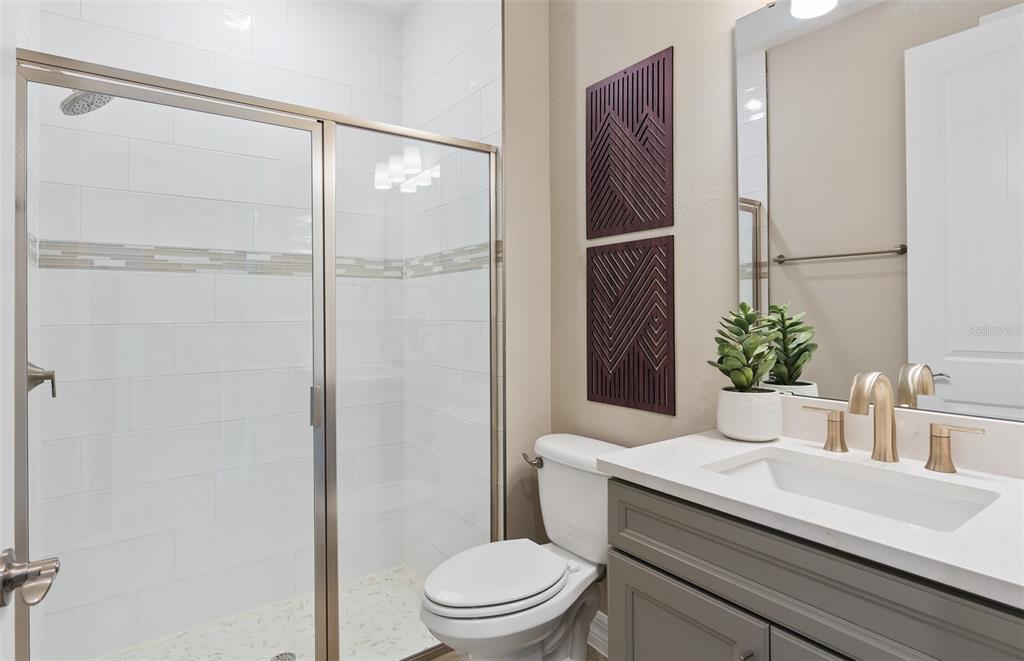 A bathroom features a glass-enclosed shower, a white toilet, and a gray vanity with gold fixtures — 6812 WILLOW BANK DRIVE, CLERMONT, FL