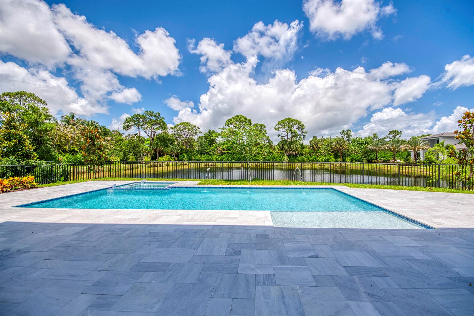 A rectangular swimming pool with a tanning ledge sits on a patio overlooking a pond — 18409 Symphony Court, Jupiter FL 33458, JUPITER, FL