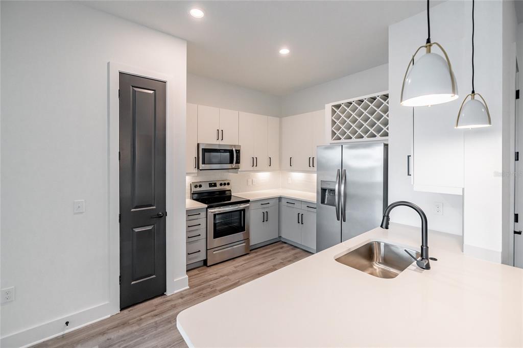A modern kitchen features white cabinets, stainless steel appliances, a wine rack, and a gray door — 1420 LAKEFRONT DRIVE UNIT 3105, SARASOTA, FL