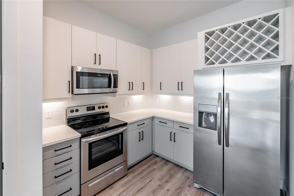 A kitchen with white cabinets, stainless steel appliances, a wine rack, and light wood flooring — 1420 LAKEFRONT DRIVE UNIT 3105, SARASOTA, FL