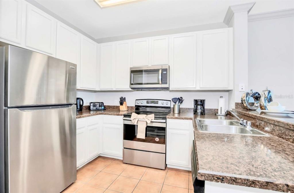 A kitchen features white cabinets, stainless steel appliances, and brown granite countertops — 14200 AVALON ROAD UNIT 411, WINTER GARDEN, FL