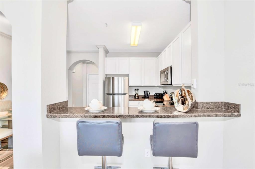 A kitchen with white cabinets and stainless steel appliances overlooks a breakfast bar with stools — 14200 AVALON ROAD UNIT 411, WINTER GARDEN, FL