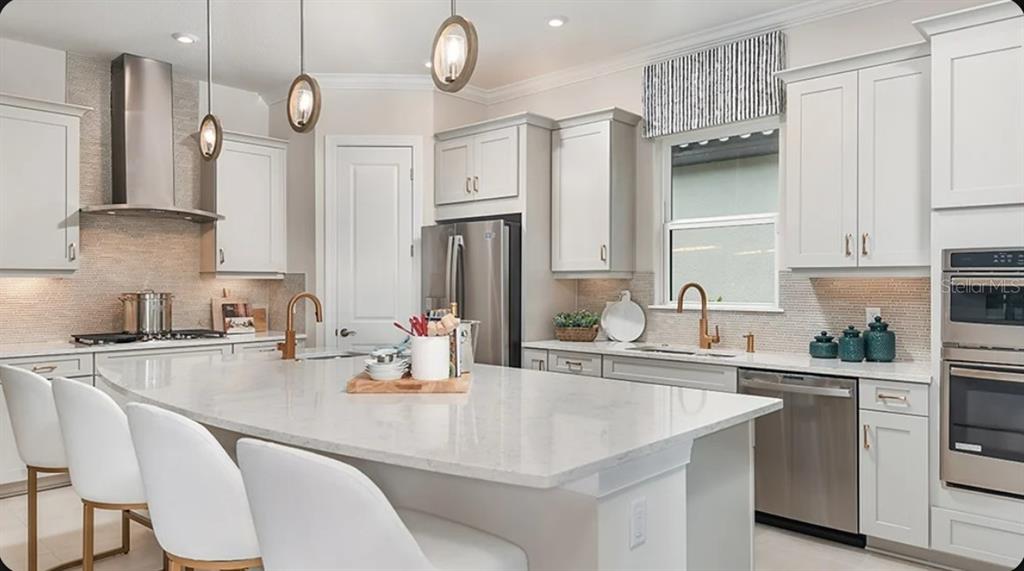 A modern kitchen features white cabinets, a large quartz island, and stainless steel appliances — 3204 VICENZA COURT, BRADENTON, FL