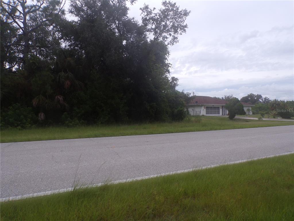 A paved road runs in front of a wooded lot next to a residential house — PONCE DE LEON BOULEVARD, NORTH PORT, FL