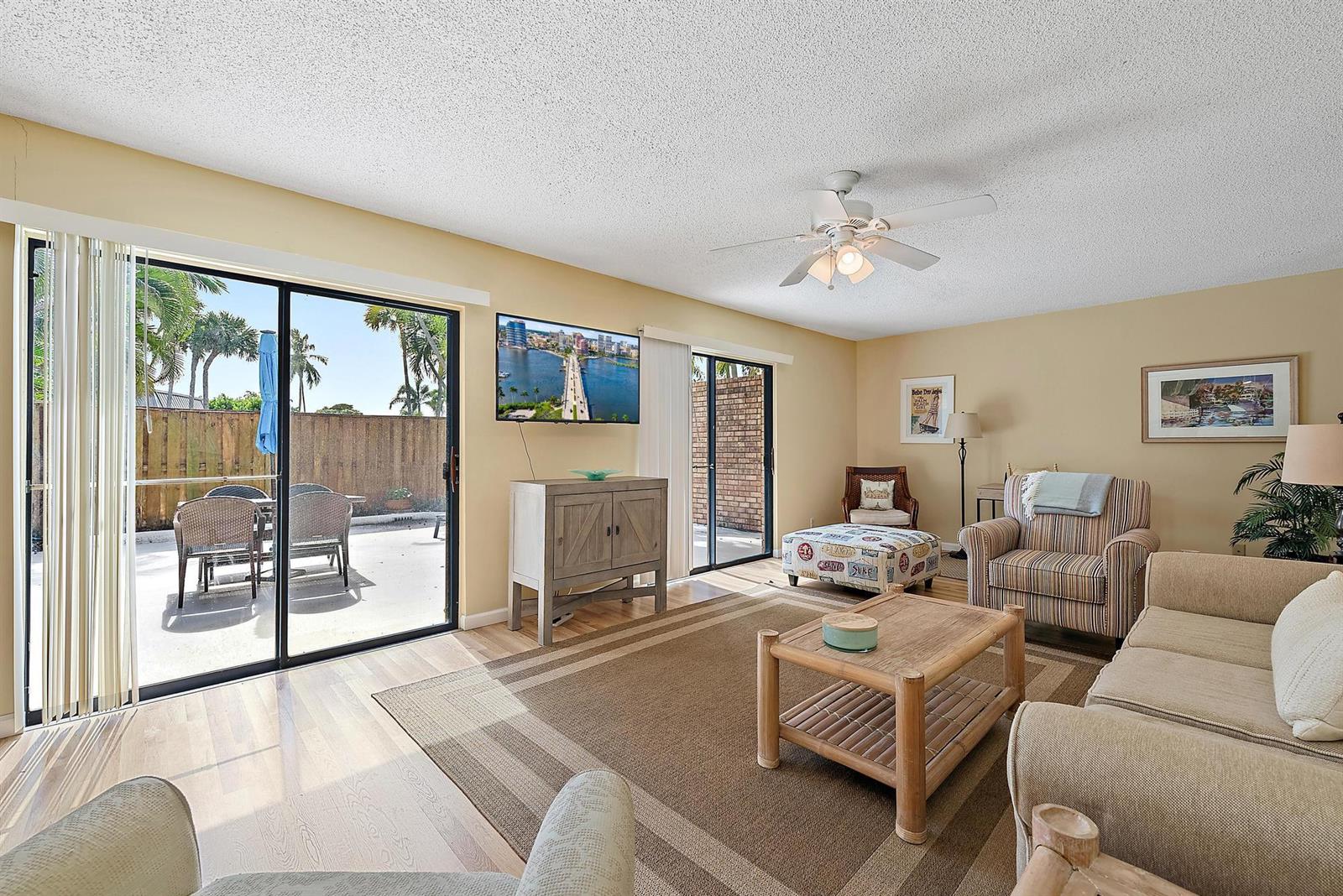 A living room features a beige sofa, patterned armchair, bamboo coffee table, and sliding glass doors — 1420 Ocean Way # 28c, Jupiter FL 33477, JUPITER, FL