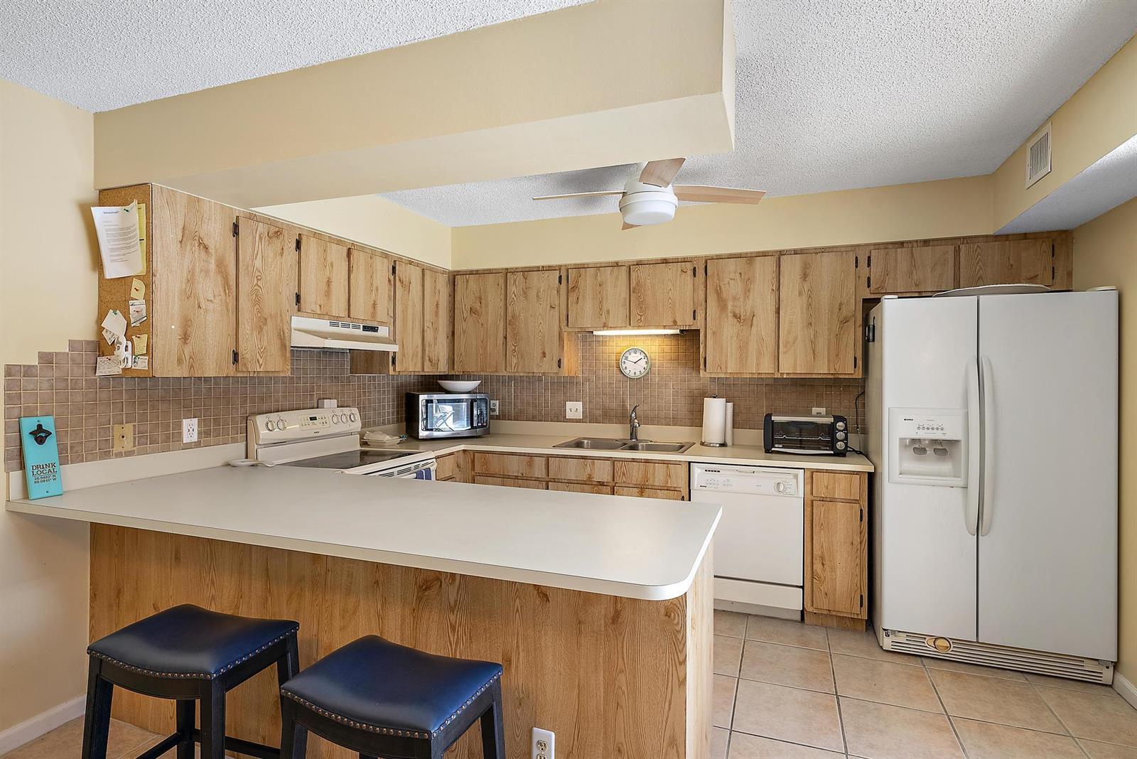 A kitchen with wood cabinets, white appliances, a breakfast bar, and tiled backsplash — 1420 Ocean Way # 28c, Jupiter FL 33477, JUPITER, FL