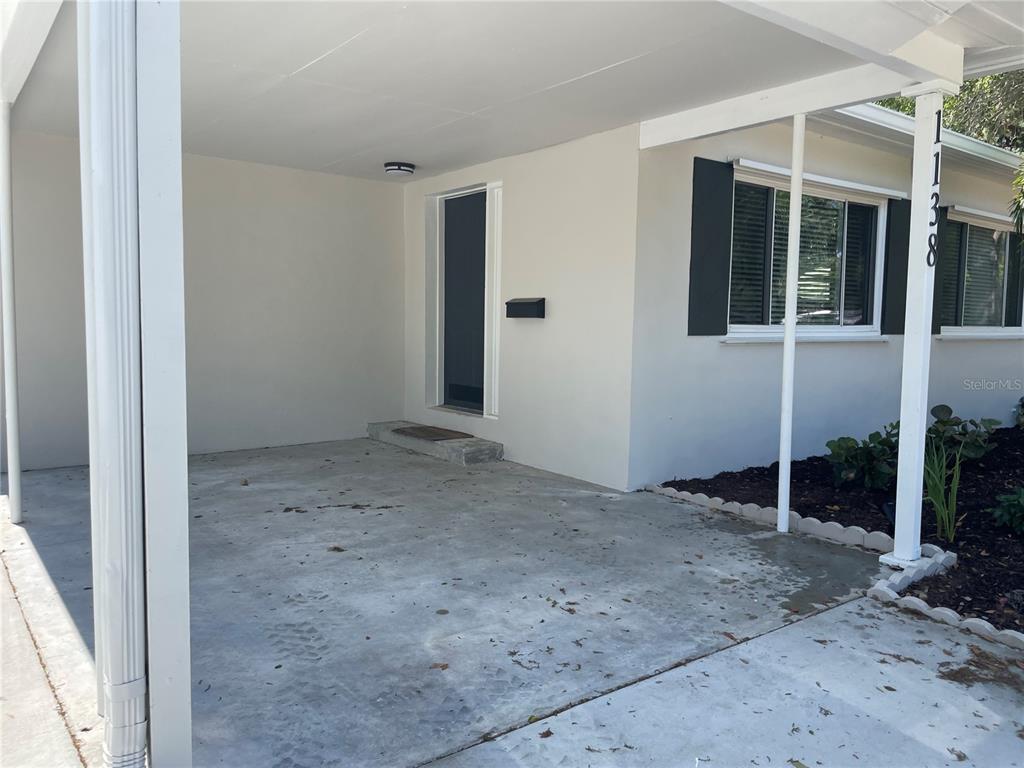 A concrete carport leads to the front entrance of a house with light-colored exterior walls — 1138 51ST AVENUE N, ST PETERSBURG, FL