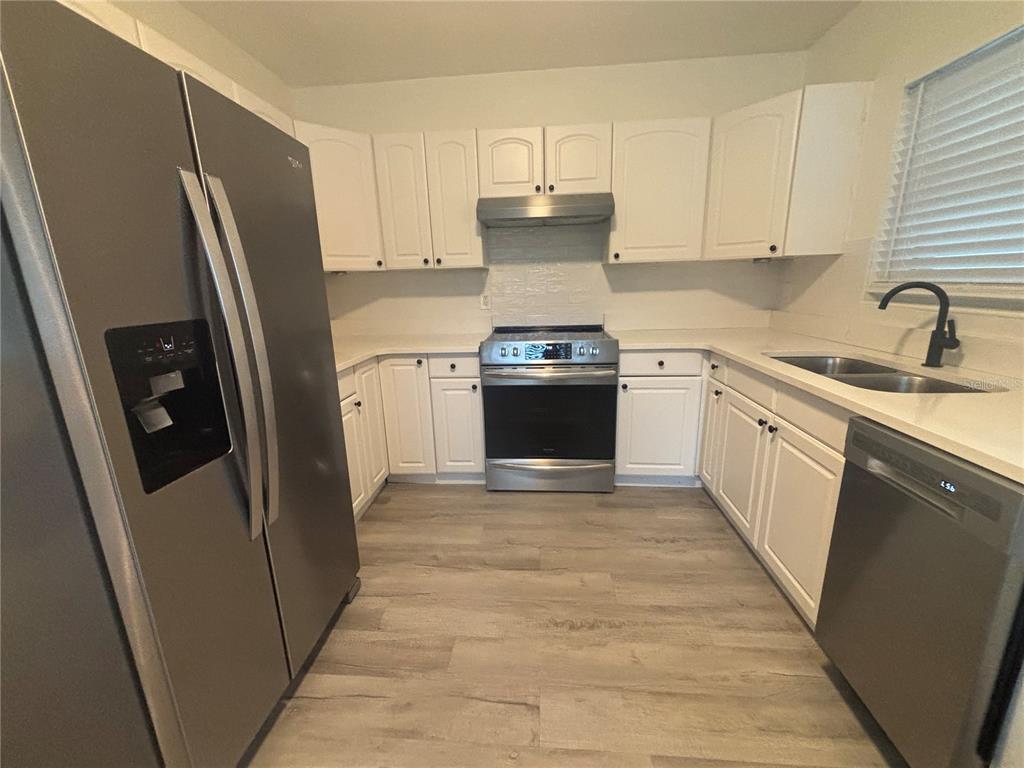 A kitchen features white cabinets, stainless steel appliances, and light wood-look flooring — 1138 51ST AVENUE N, ST PETERSBURG, FL