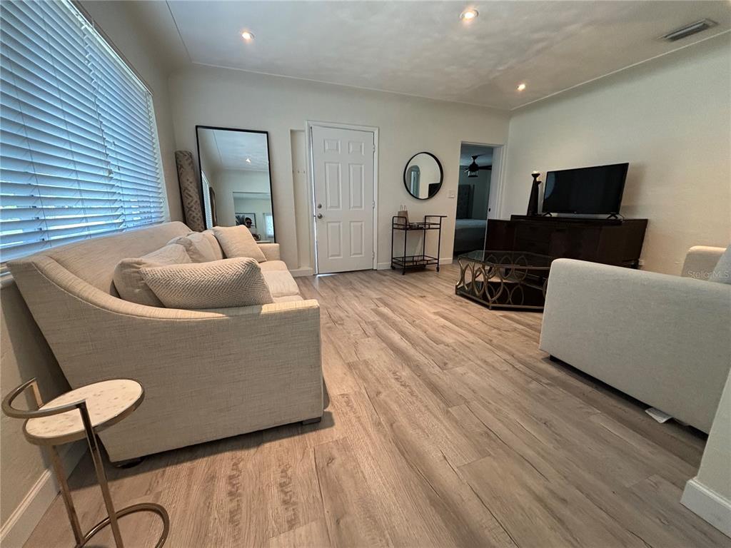 A living room features light wood-look flooring, a beige sofa, and a television console — 1138 51ST AVENUE N, ST PETERSBURG, FL
