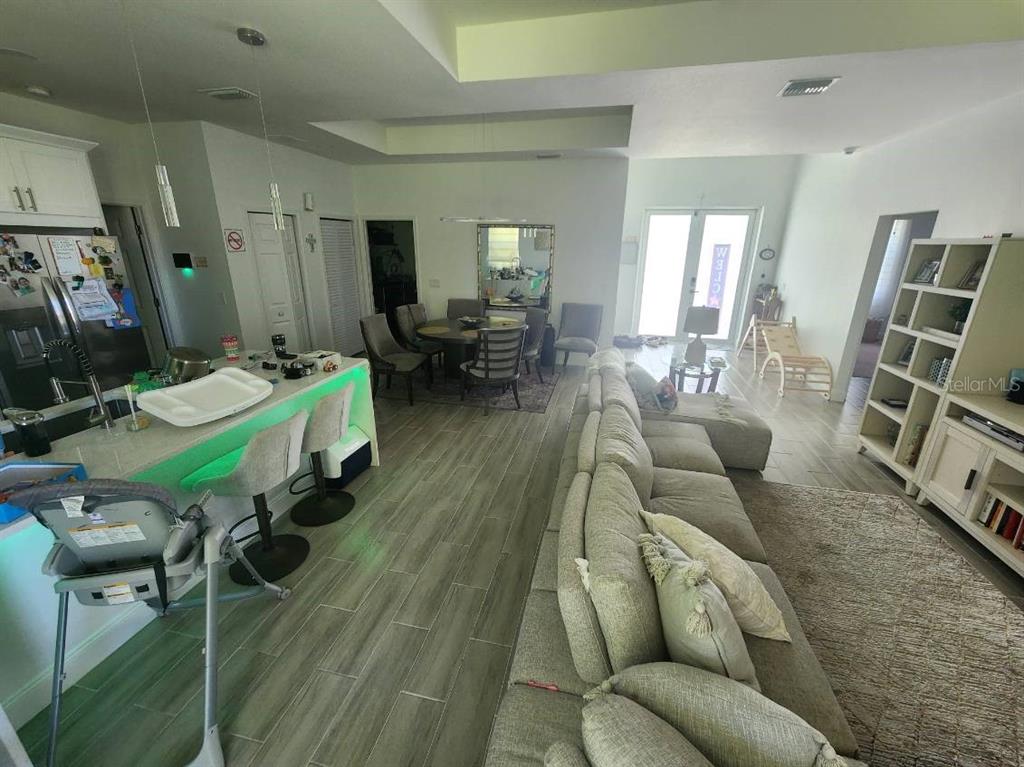 An open-concept living room and kitchen area features tile flooring, a sectional sofa, and dining — 1405 UNICE AVENUE N, LEHIGH ACRES, FL