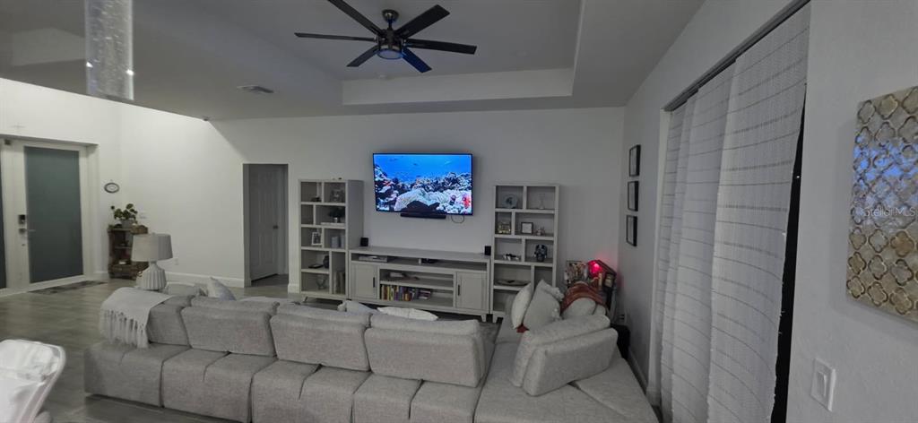 A living room features a large sectional sofa, a wall-mounted television, and white shelving units — 1405 UNICE AVENUE N, LEHIGH ACRES, FL