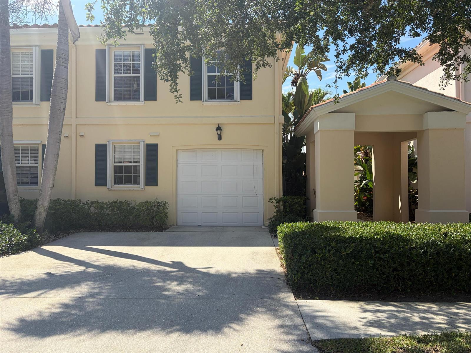 A two-story yellow townhouse features a white garage door, dark shutters, and a covered entryway — 2136 Tigris Drive, West Palm Beach FL 33411, WEST PALM BEACH, FL