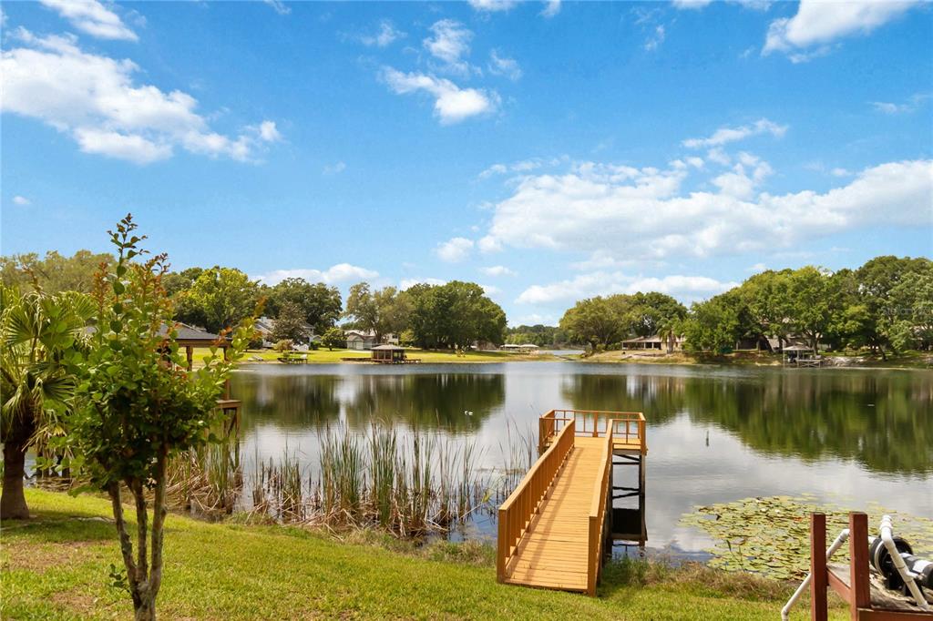 A wooden dock extends into a calm lake surrounded by trees and grassy lawns — 9835 LAKESHORE DRIVE, CLERMONT, FL