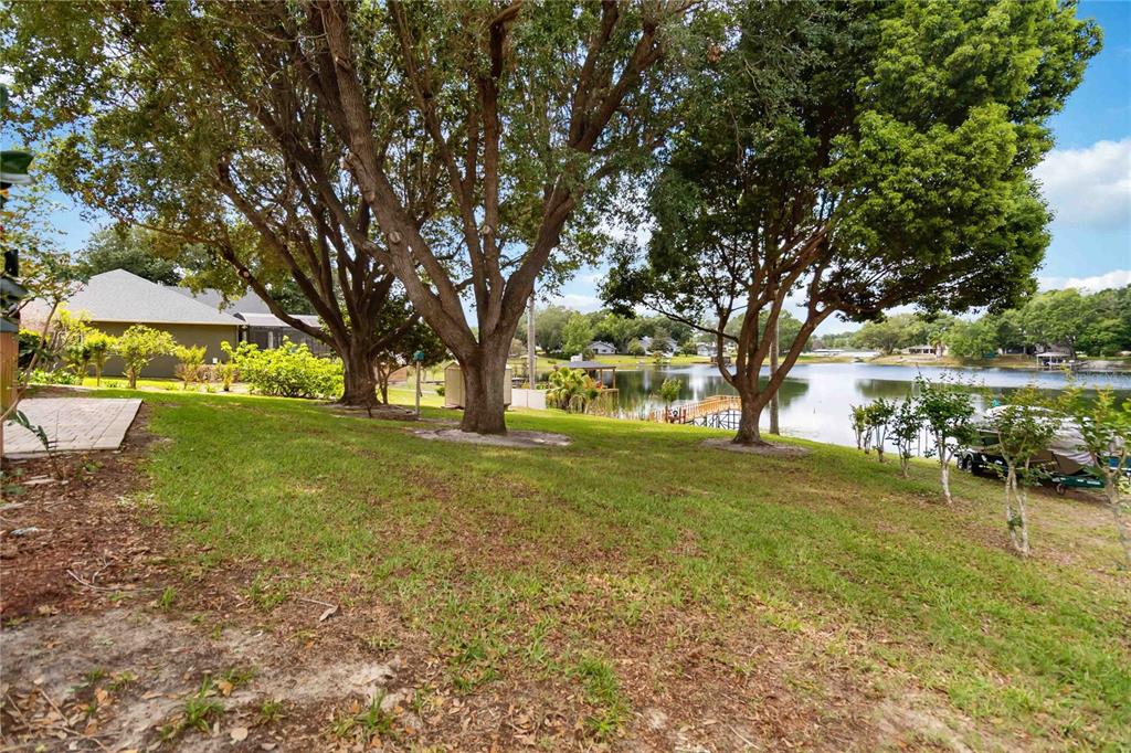 A grassy backyard features large shade trees overlooking a lake with a boat dock — 9835 LAKESHORE DRIVE, CLERMONT, FL