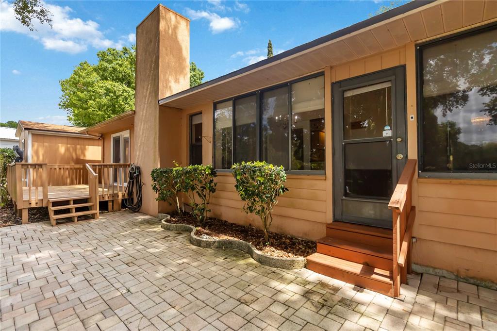 A tan house exterior features a brick patio, a wooden deck, and a glass door — 9835 LAKESHORE DRIVE, CLERMONT, FL