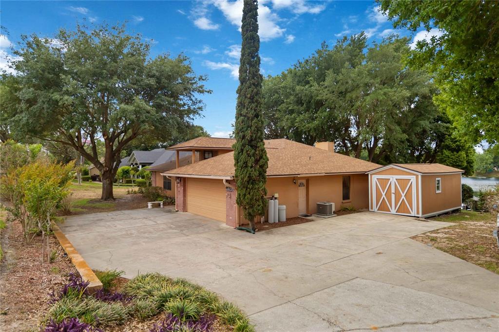 A single-story house with a tan exterior, a two-car garage, and a detached storage shed — 9835 LAKESHORE DRIVE, CLERMONT, FL