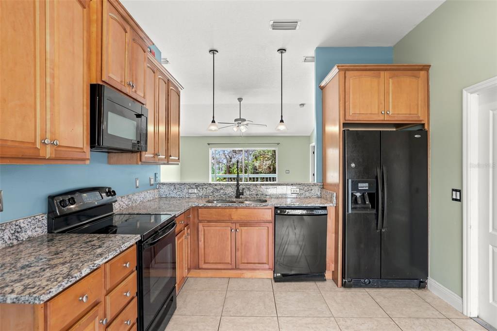 A kitchen features wood cabinets, black appliances, granite countertops, and light-colored tile flooring — 2063 MONTEREY DRIVE, DELTONA, FL