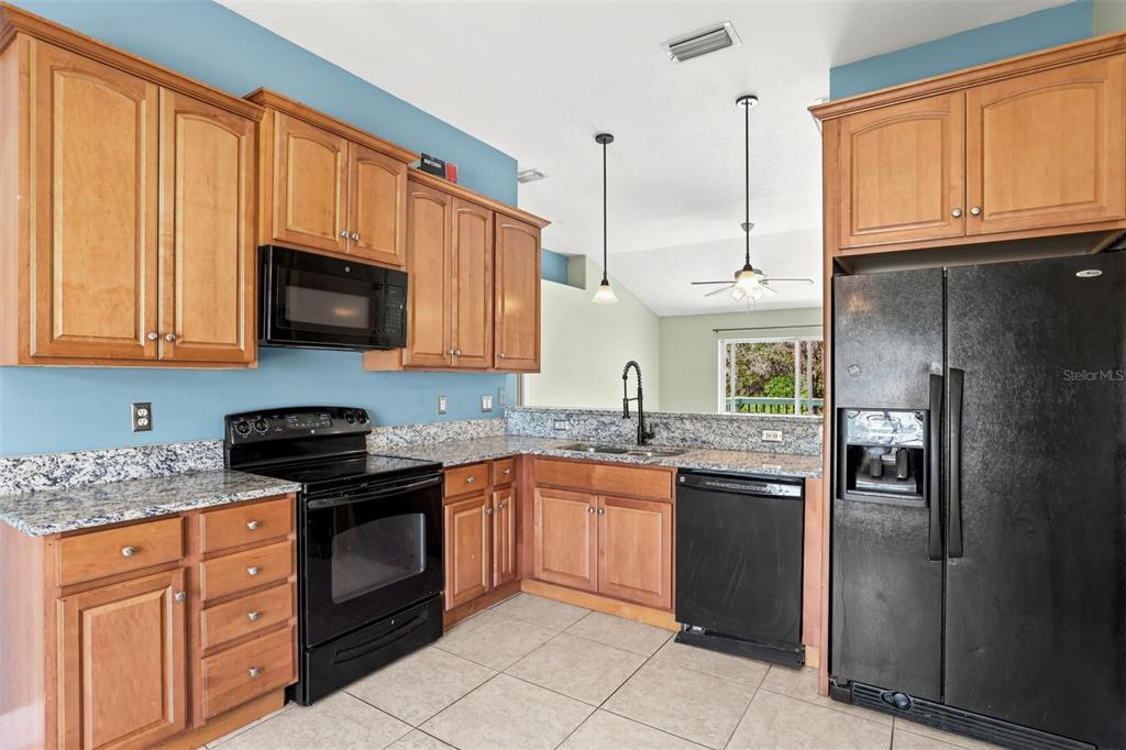 A kitchen features wood cabinets, granite countertops, black appliances, and light-colored tile flooring — 2063 MONTEREY DRIVE, DELTONA, FL