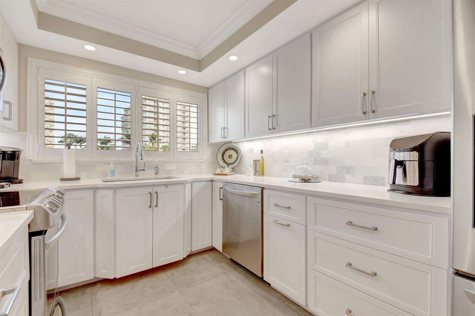 A modern kitchen features white cabinetry, stainless steel appliances, marble backsplash, and plantation window shutters — 3224 S Ocean Boulevard # 214, Highland Beach FL 33487, HIGHLAND BEACH, FL