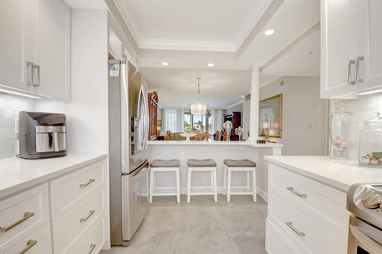 A white kitchen with stainless steel appliances and a breakfast bar overlooking a living area — 3224 S Ocean Boulevard # 214, Highland Beach FL 33487, HIGHLAND BEACH, FL