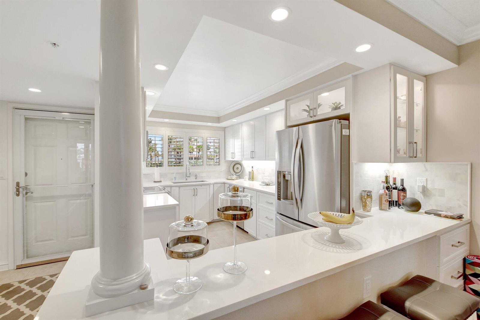 A modern kitchen features white cabinetry, stainless steel appliances, and a white quartz breakfast bar — 3224 S Ocean Boulevard # 214, Highland Beach FL 33487, HIGHLAND BEACH, FL