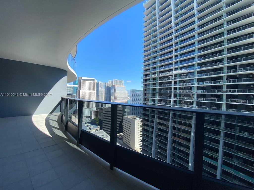 A curved balcony overlooks a dense urban skyline with tall glass skyscrapers under a clear sky — 1000 Brickell Plz # 3207, Miami FL 33131, MIAMI, FL