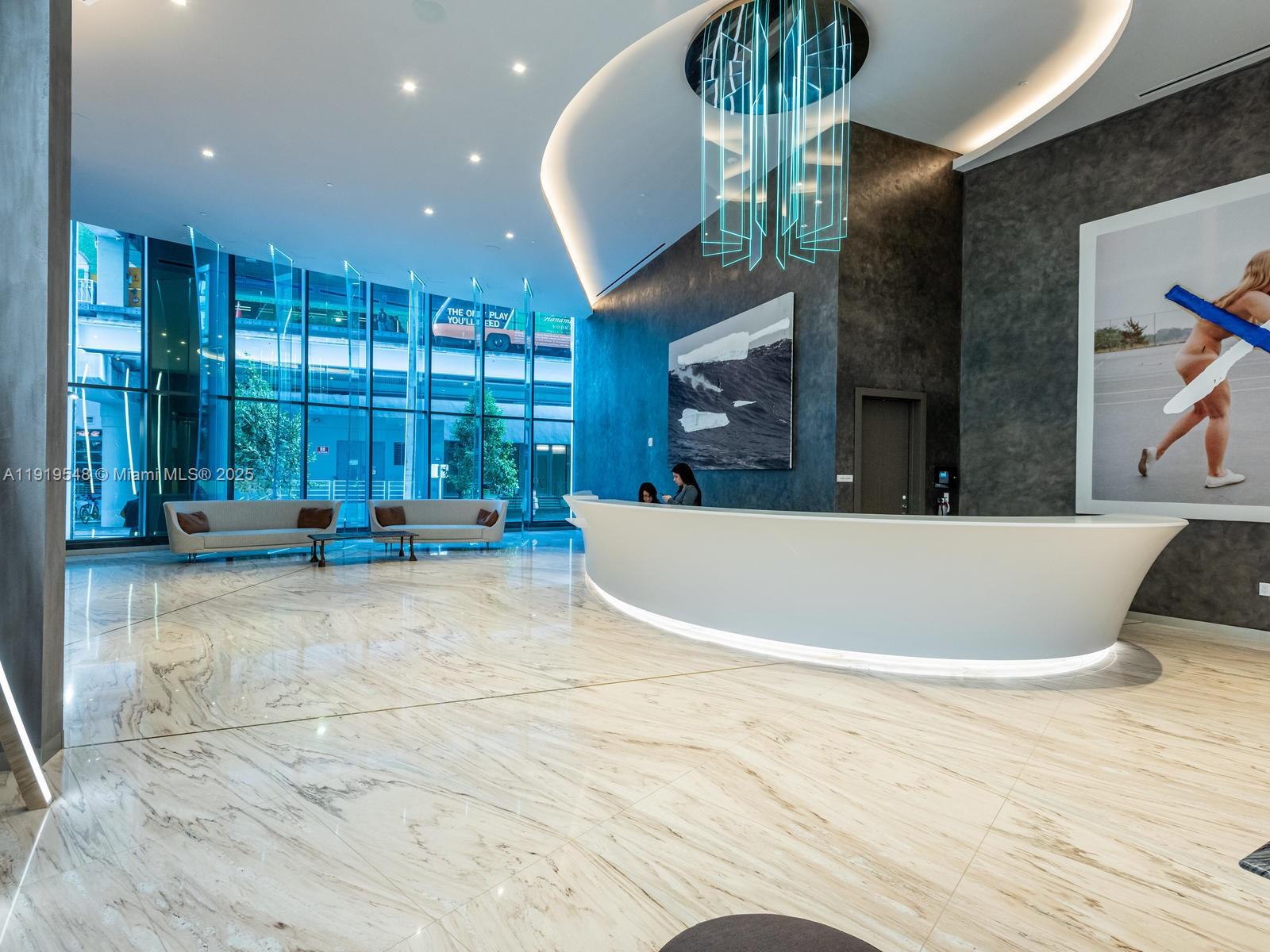 A modern lobby features a curved white reception desk, marble floors, and floor-to-ceiling windows — 1000 Brickell Plz # 3207, Miami FL 33131, MIAMI, FL