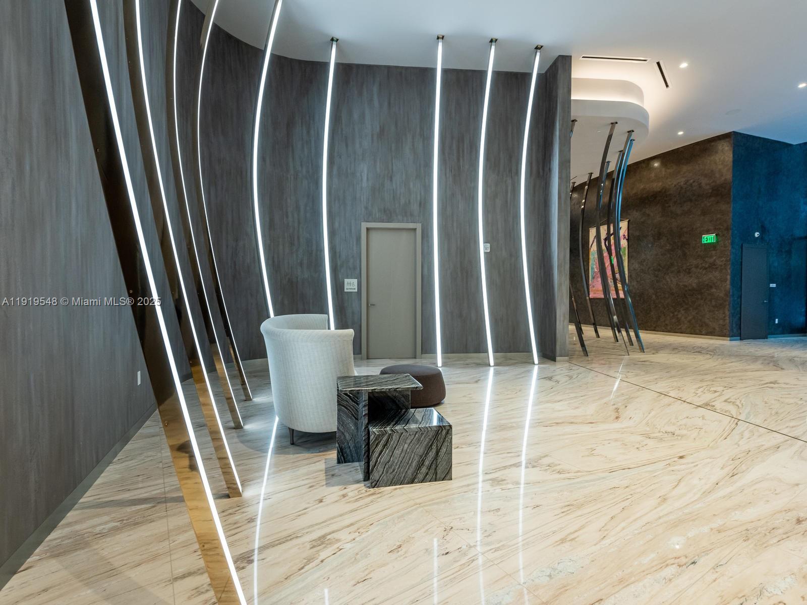 A modern lobby features curved walls with vertical lighting, marble flooring, and a lounge chair — 1000 Brickell Plz # 3207, Miami FL 33131, MIAMI, FL