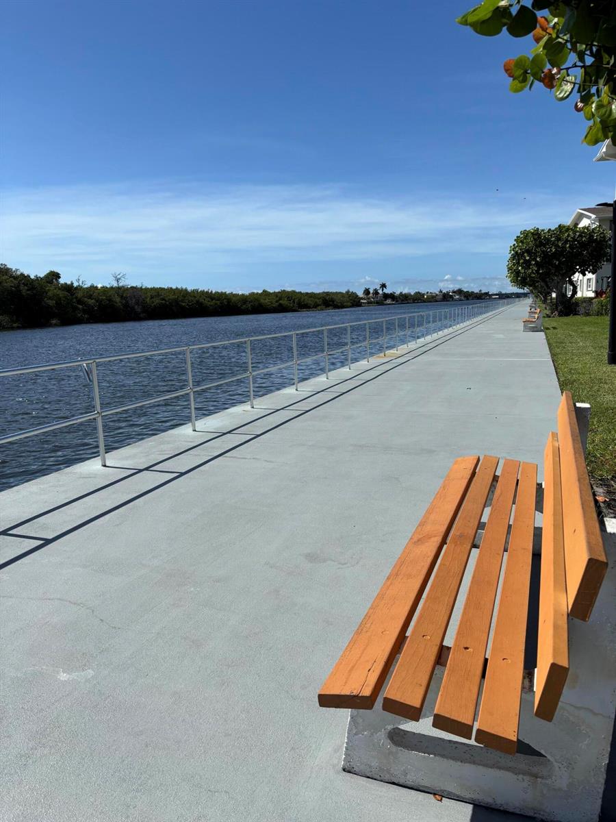 A wooden bench sits on a concrete walkway beside a metal railing and a canal — 210 Horizons E # 107, Boynton Beach FL 33435, BOYNTON BEACH, FL