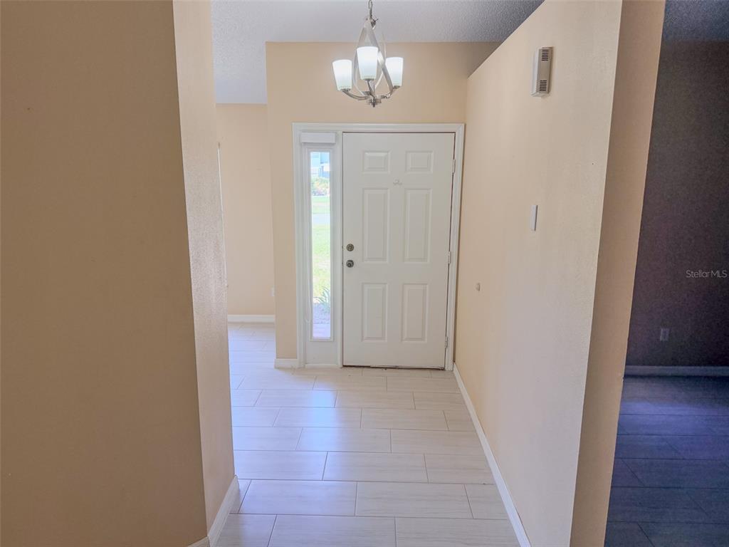 An entryway features light-colored tile flooring, a white front door with a sidelight, and a chandelier — 770 AMERICANA COURT, KISSIMMEE, FL