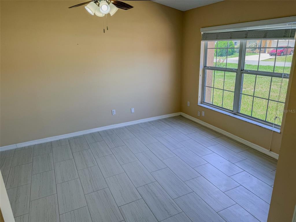 An empty room features light-colored tile flooring, beige walls, a ceiling fan, and a window — 770 AMERICANA COURT, KISSIMMEE, FL