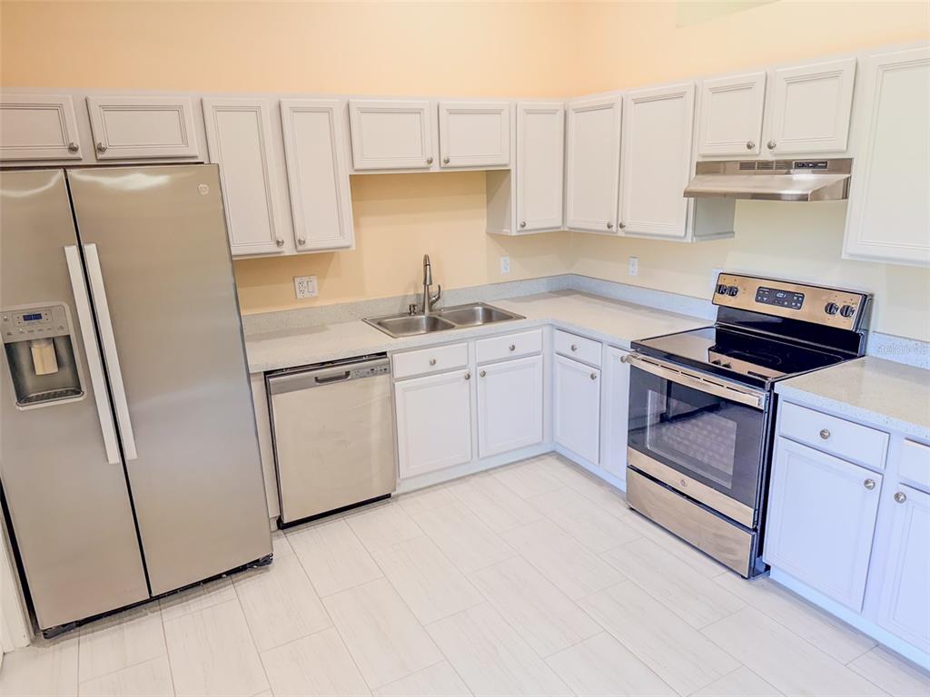 A kitchen with white cabinets, stainless steel appliances, light countertops, and light-colored tile flooring — 770 AMERICANA COURT, KISSIMMEE, FL