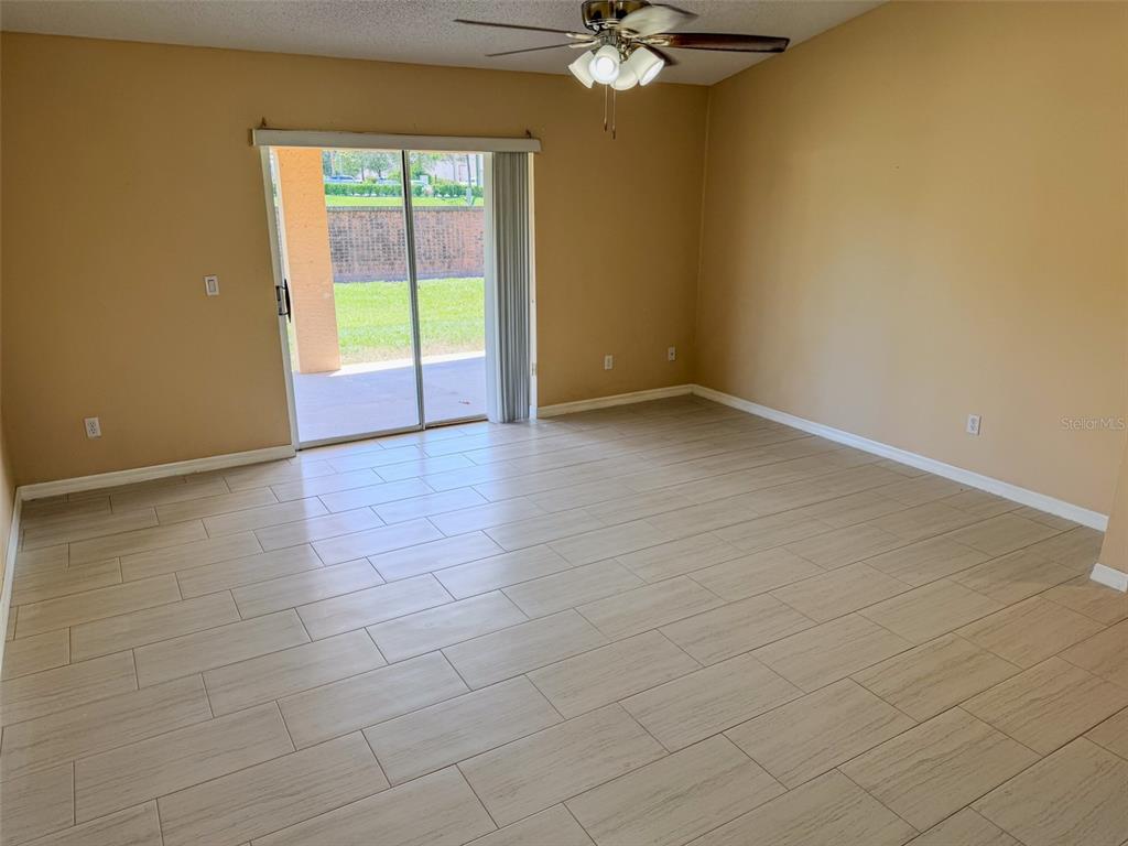 An empty room features light-colored wood-look tile flooring, tan walls, and a sliding glass door — 770 AMERICANA COURT, KISSIMMEE, FL