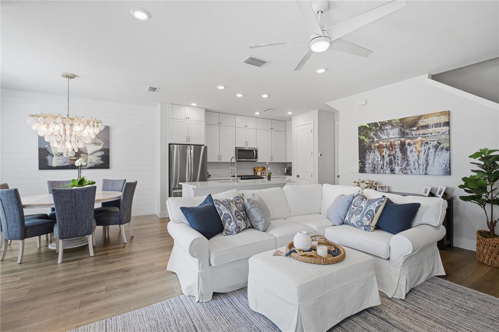 An open-concept living and dining area features a white sectional sofa, kitchen, and wood flooring — 7221 SUTTON LANE, SARASOTA, FL