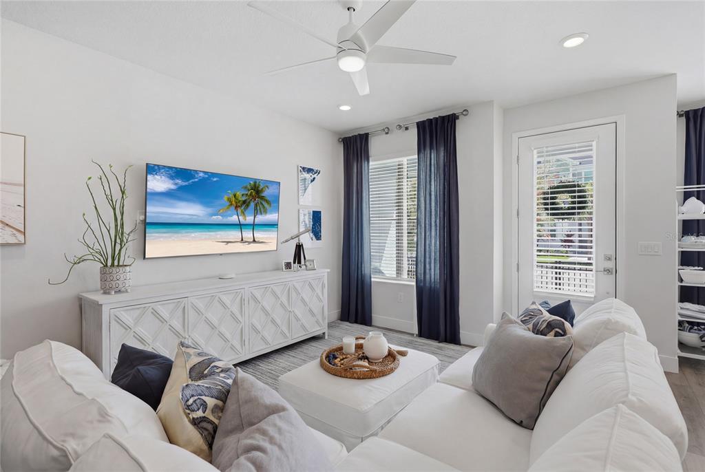 A bright living room features a white sectional sofa, a media console, and dark curtains — 7221 SUTTON LANE, SARASOTA, FL