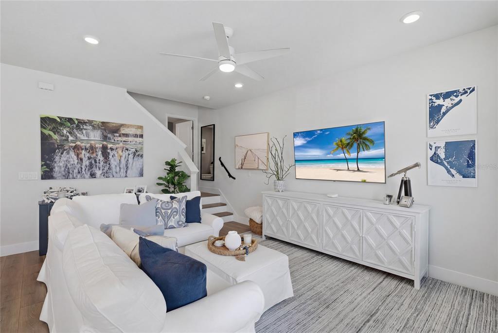 A bright living room features a white sectional sofa, a television, and a media console — 7221 SUTTON LANE, SARASOTA, FL
