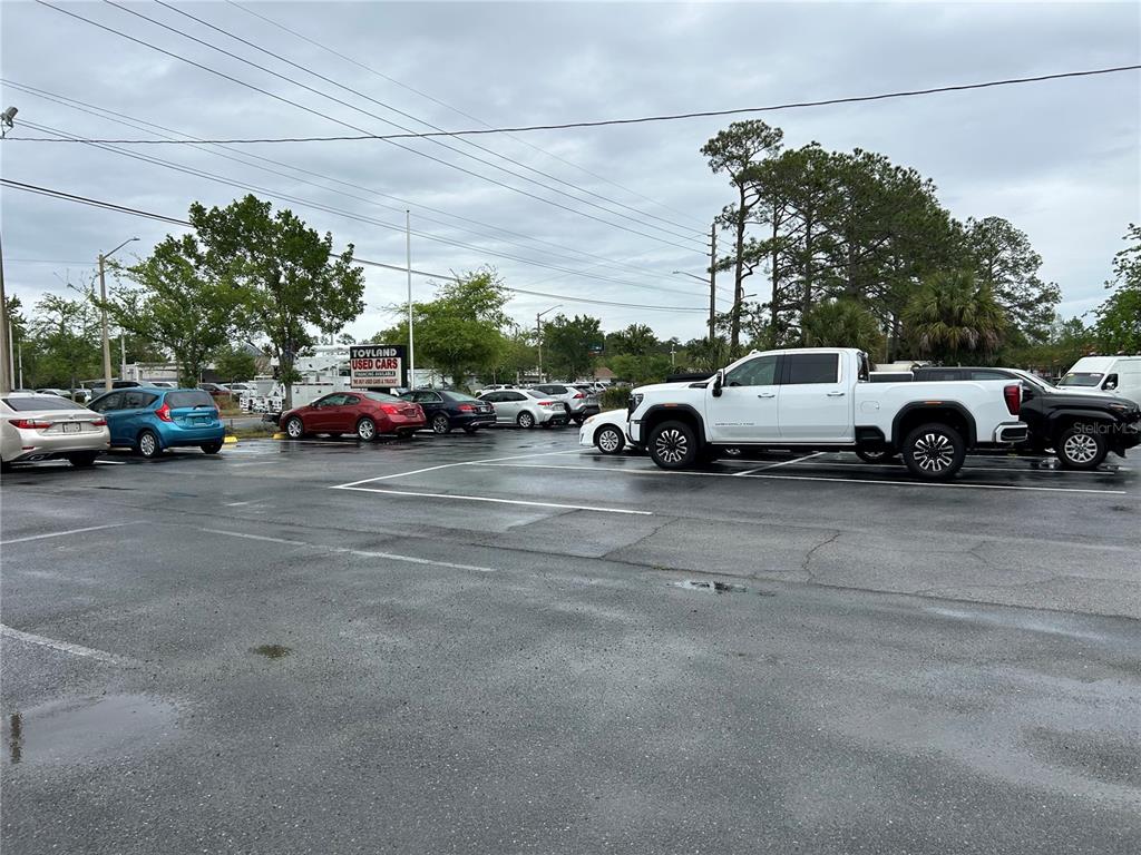 A paved parking lot features several parked vehicles and a sign for Toyland Used Cars — 241 NE 39TH AVENUE, GAINESVILLE, FL