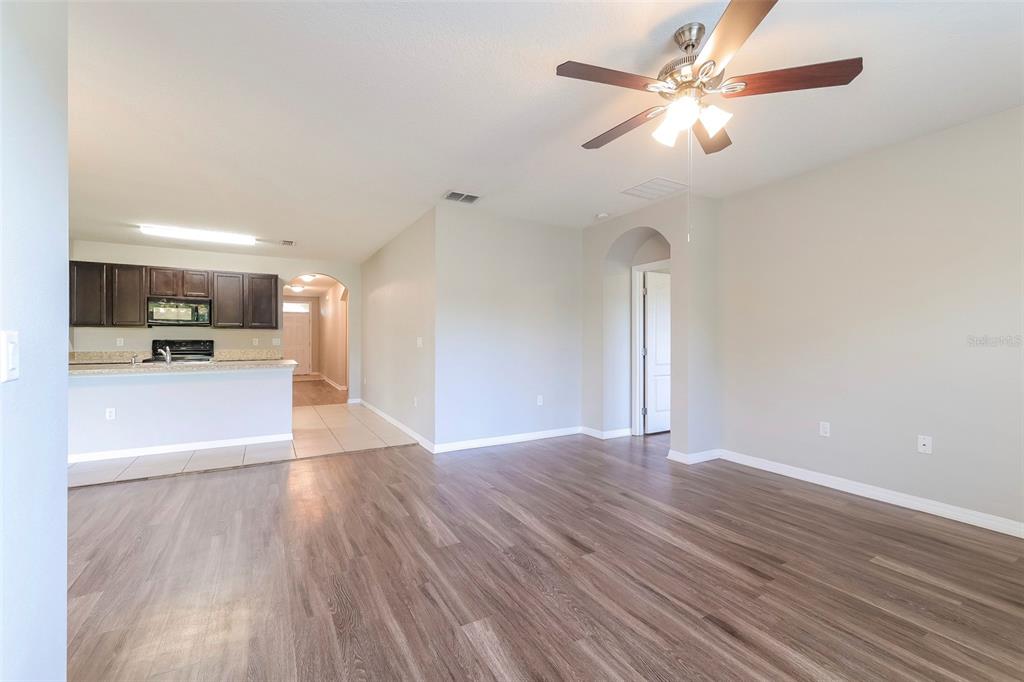 A living room with wood-look flooring, a ceiling fan, and an adjacent open kitchen — 2330 SEQUOIA WAY, DAVENPORT, FL
