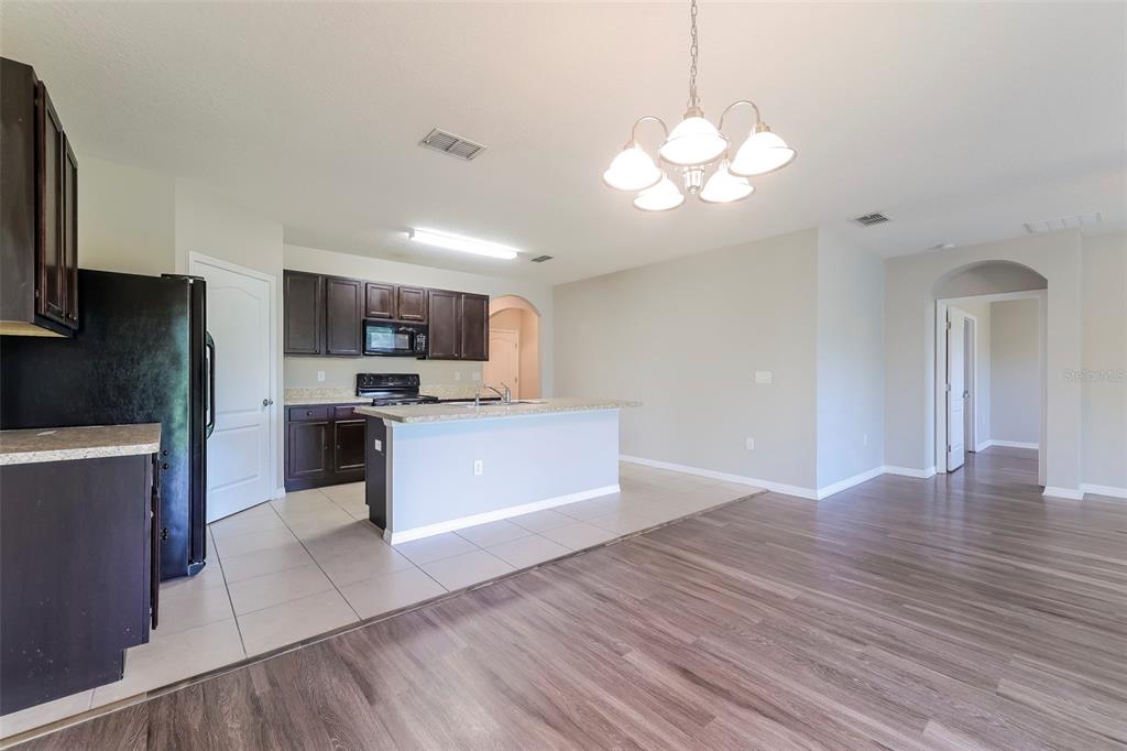 A kitchen with dark cabinetry and a central island opens to a wood-floored living area — 2330 SEQUOIA WAY, DAVENPORT, FL