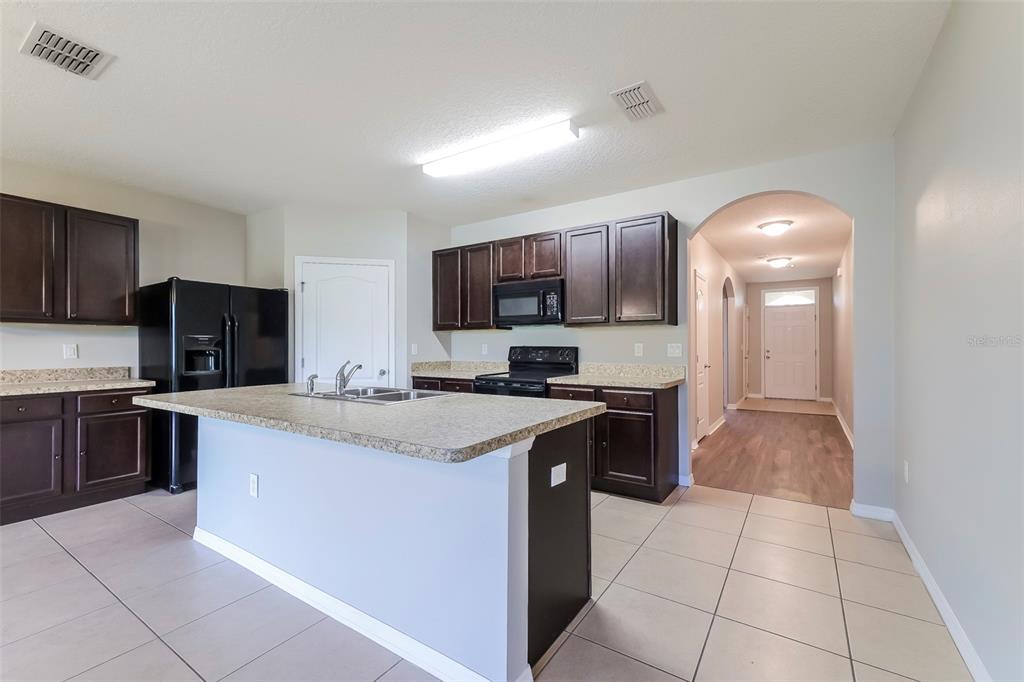 A kitchen features dark wood cabinets, granite countertops, a central island, and tile flooring — 2330 SEQUOIA WAY, DAVENPORT, FL
