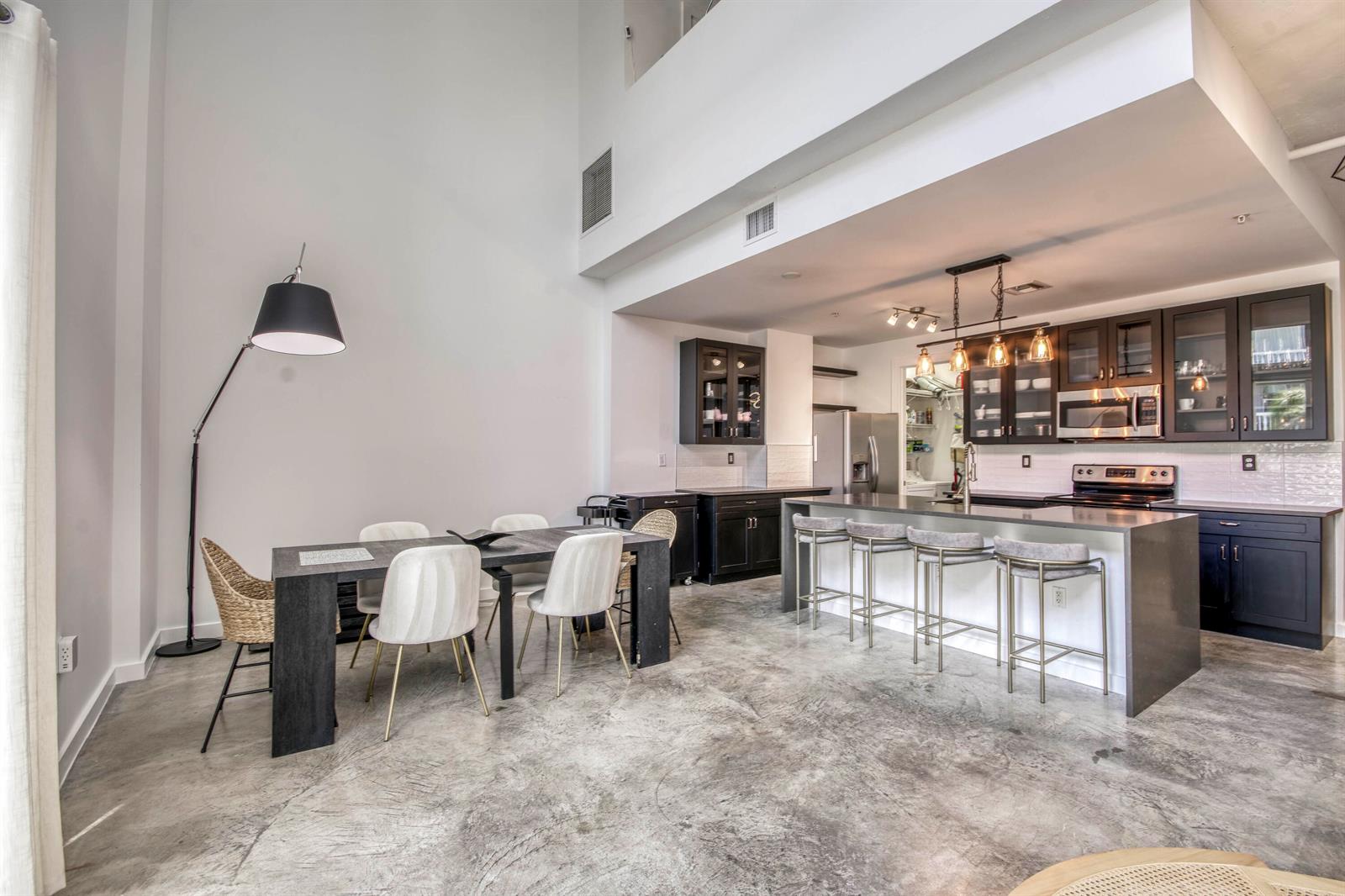 A modern kitchen and dining area features dark cabinetry, a kitchen island, and concrete floors — 108 Lake Avenue # 202, FL 33460, FL