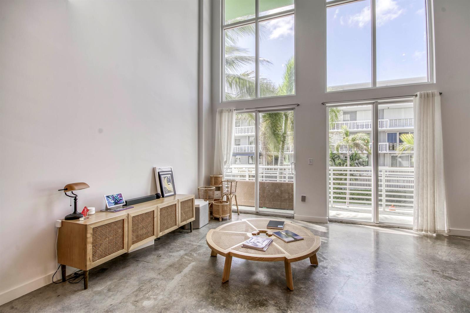 A living room with high ceilings, concrete floors, a rattan media console, and large windows — 108 Lake Avenue # 202, FL 33460, FL