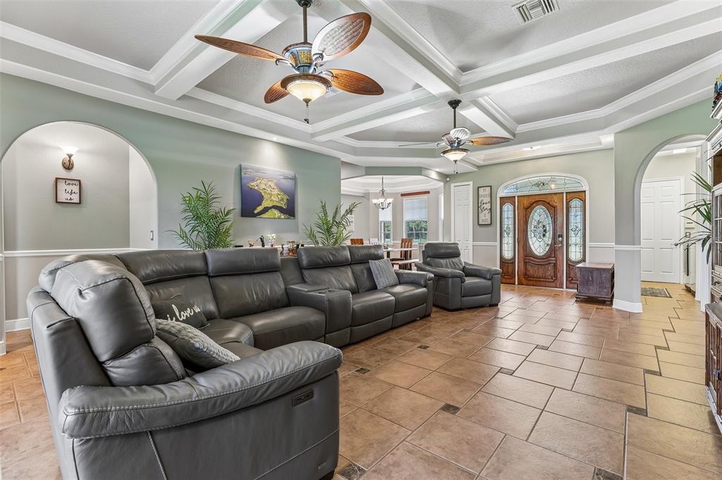 A spacious living room features a large grey sectional, tile flooring, and coffered ceilings — 30418 ISLAND CLUB DRIVE, DEER ISLAND, FL