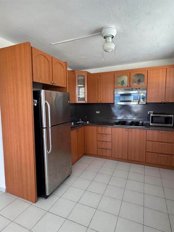 A kitchen features wood cabinets, stainless steel appliances, and light-colored tile flooring — Calle 21, Lote 755, BARRIO SANTA MARIA, VILLA BORINQUEN, VIEQUES, PR